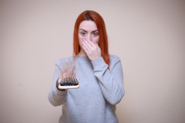 una mujer mira un cepillo lleno de pelo