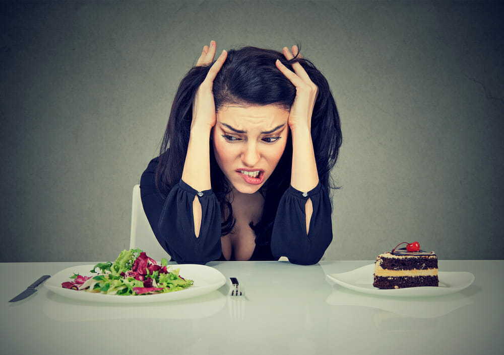 una mujer se sienta en una mesa con un plato de tarta y otro de ensalada