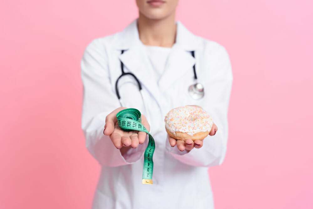  El médico sostiene un donut con glaseado en una mano y un centímetro en la otra