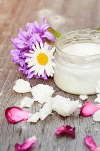 Aceite de coco en un frasco, junto a pétalos de flores