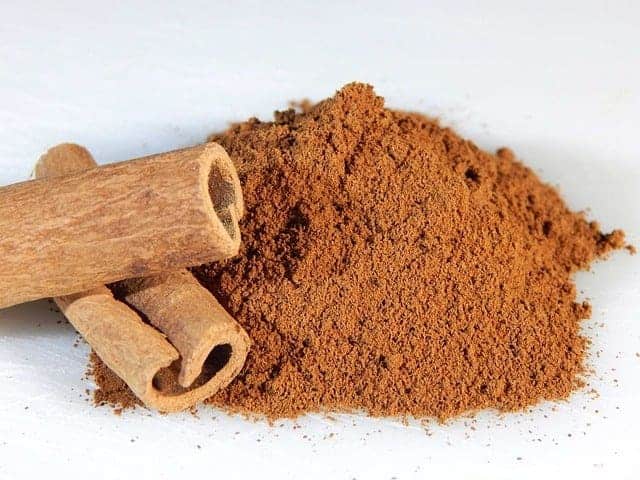 Canela molida, junto a una rama de canela
