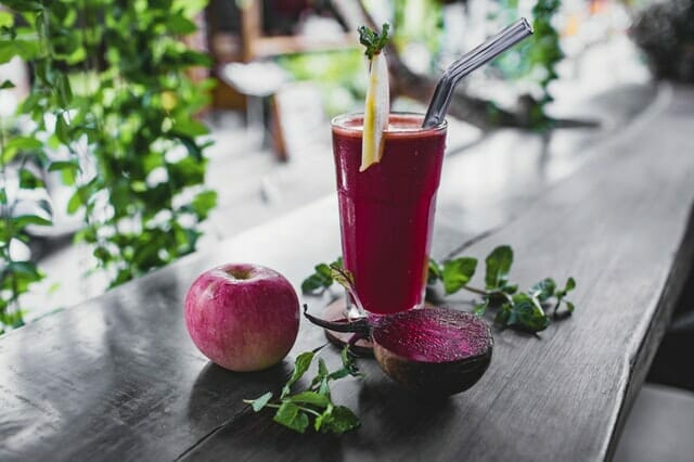 Zumo de remolacha en un vaso, junto a una manzana y una remolacha