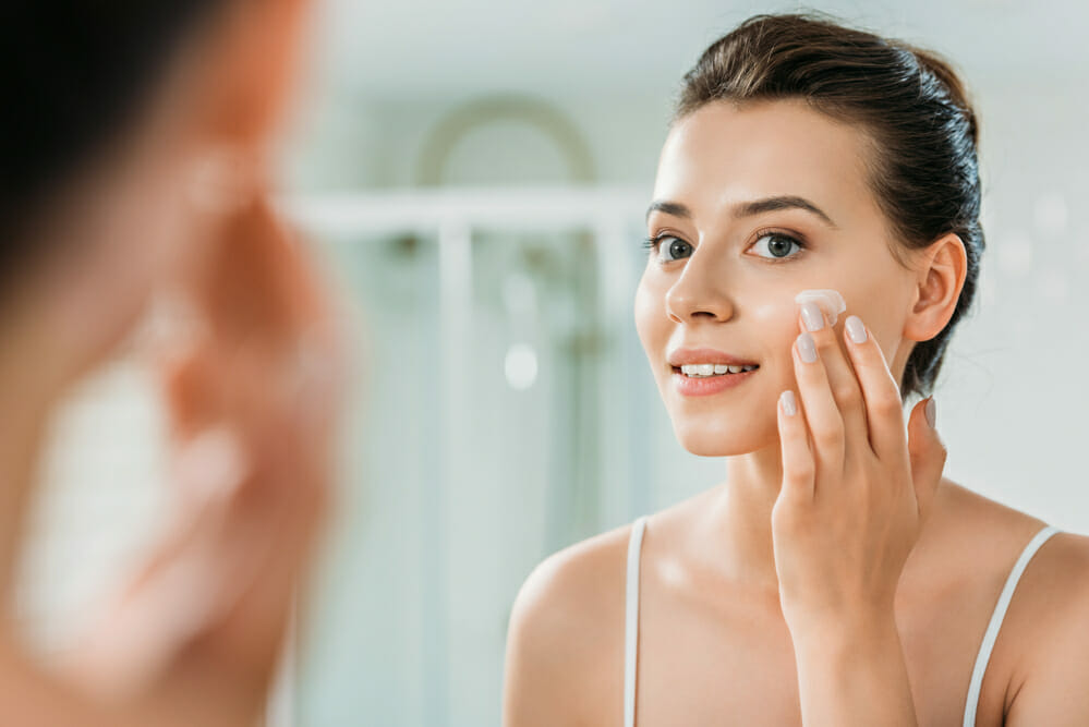 una mujer se da palmaditas con la crema en las mejillas