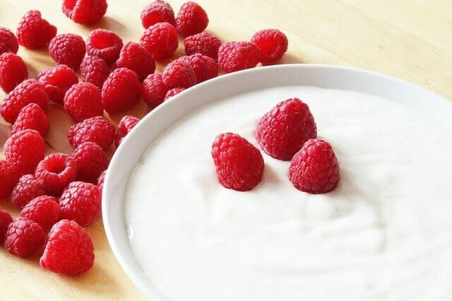  yogur en un bol, junto a una frambuesa