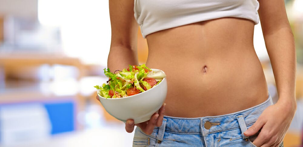 una mujer delgada sostiene una ensaladera de verduras